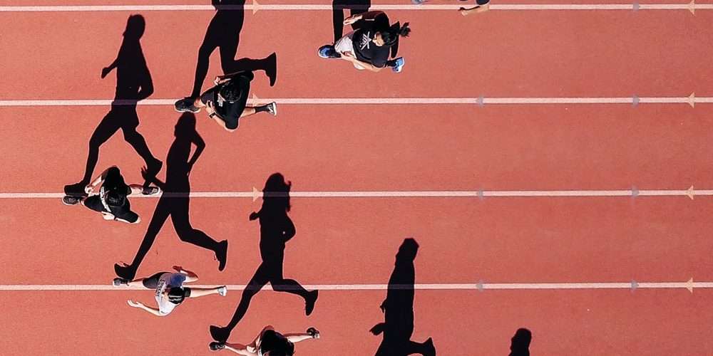 Degli atleti ripresi dall’alto corrono su una pista di atletica: la corsa è uno strumento perfetto insieme al teambuilding per rinforzare i legami e la produttività aziendale