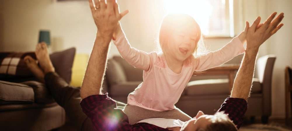 In un soggiorno un papà gioca con una bambina illuminati dal sole, la cui energia è fonte di benessere e salute