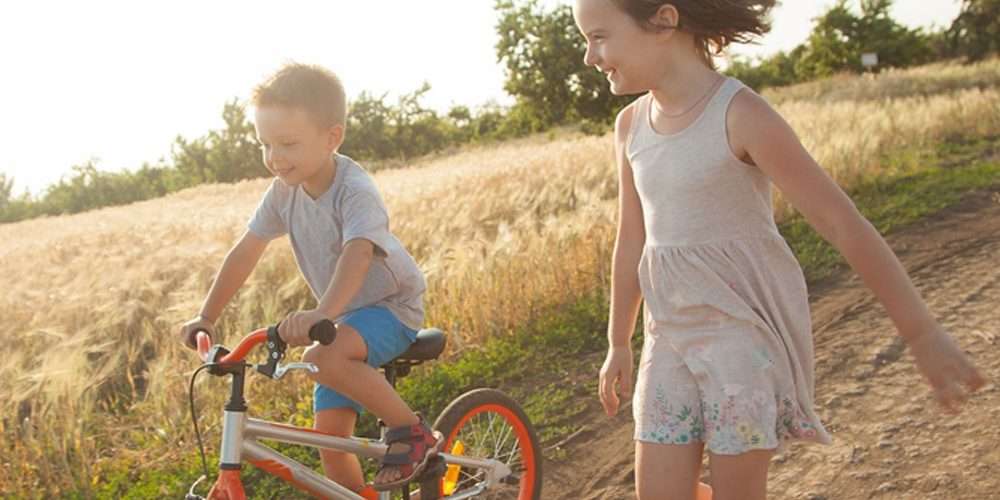 Un bambino in bici gioca con una bambina in campagna: si può viaggiare in bicicletta anche con i bambini
