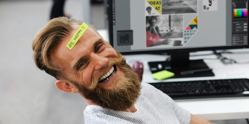 Un ragazzo sorride accanto al computer: le energie positive vanno conservate a lungo dopo il rientro al lavoro