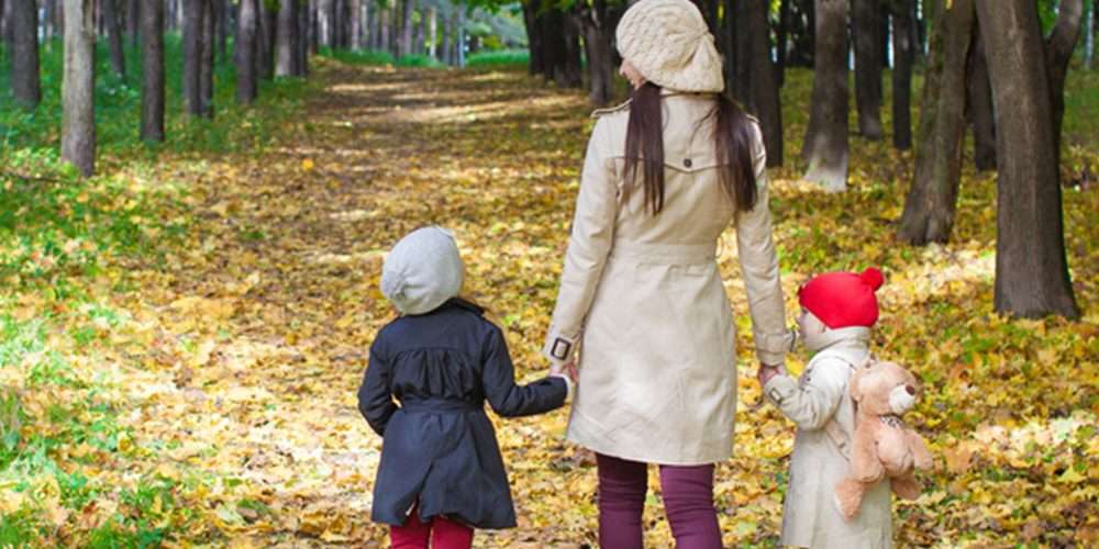 Una mamma cammina in un bosco con due bambini, tenendoli per mano e mostrando loro le maraviglie dell’ambiente