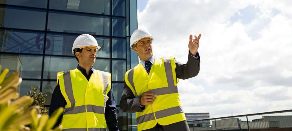 Due tecnici all’esterno di un moderno complesso edilizio discutono di attestati di certificazione energetica