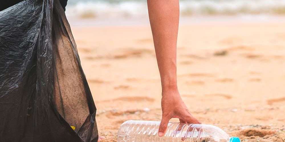 Una mano raccoglie una bottiglia di plastica in spiaggia: un gesto contro l’inquinamento marino