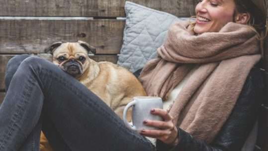 Una ragazza in una fredda giornata sorride col proprio cane sulle gambe: il buonumore non deve mai mancare in inverno