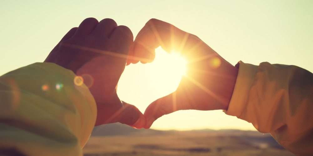 Due mani fanno il simbolo del cuore sullo sfondo di un cielo illuminato dal sole