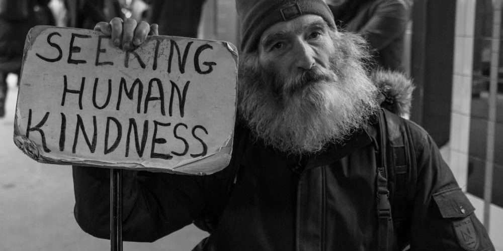 Un senzatetto con cartello chiede rispetto: la lotta alla povertà è tra gli obiettivi dell’ONU