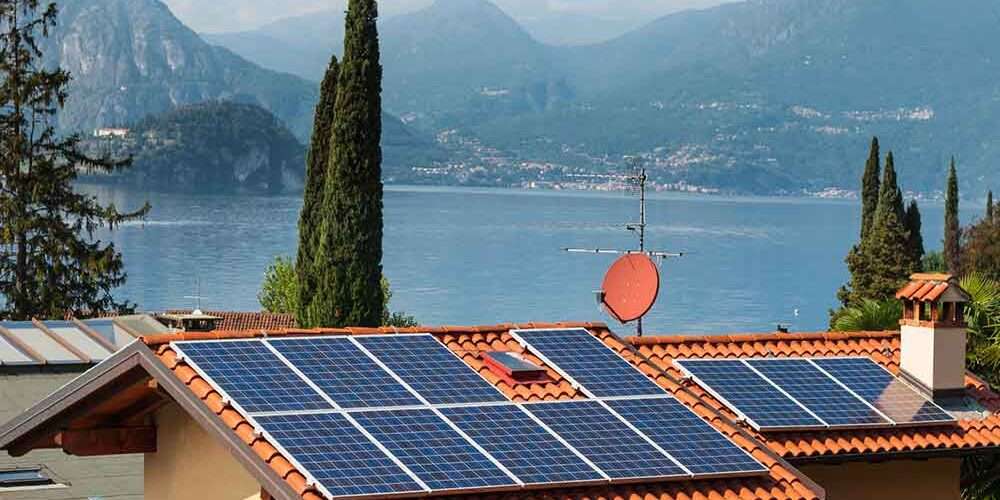 Impianto fotovoltaico sui tetti di alcune abitazioni in un paesaggio con lago sullo sfondo