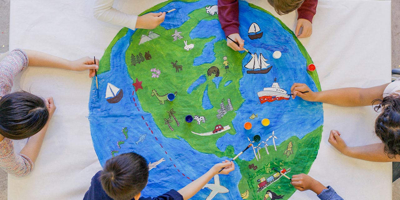 Dei bambini dipingono su un grande telo il Pianeta Terra