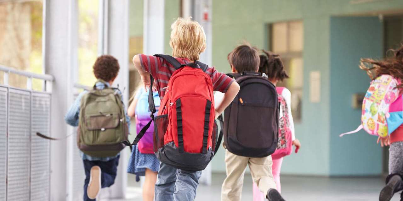 Un gruppo di ragazzi con zaini in spalla in un corridoio scolastico: il rientro a scuola può essere sostenibile con i giusti materiali