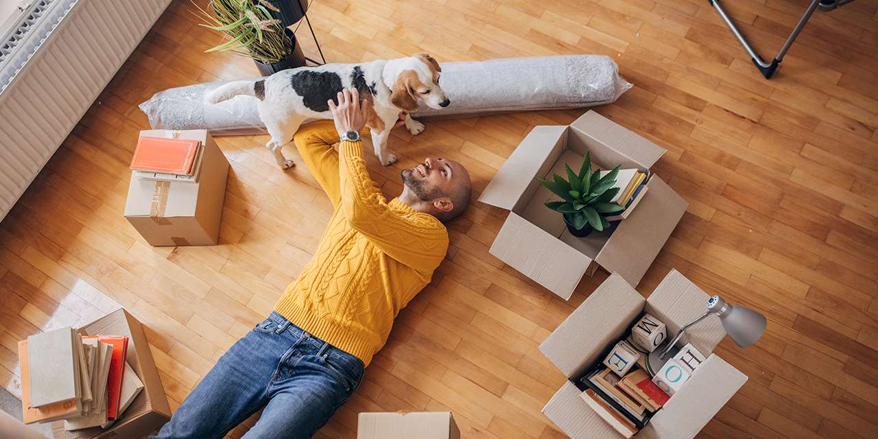 Un ragazzo disteso sul pavimento tra scatole per il trasloco gioca con un cane in un momento di relax