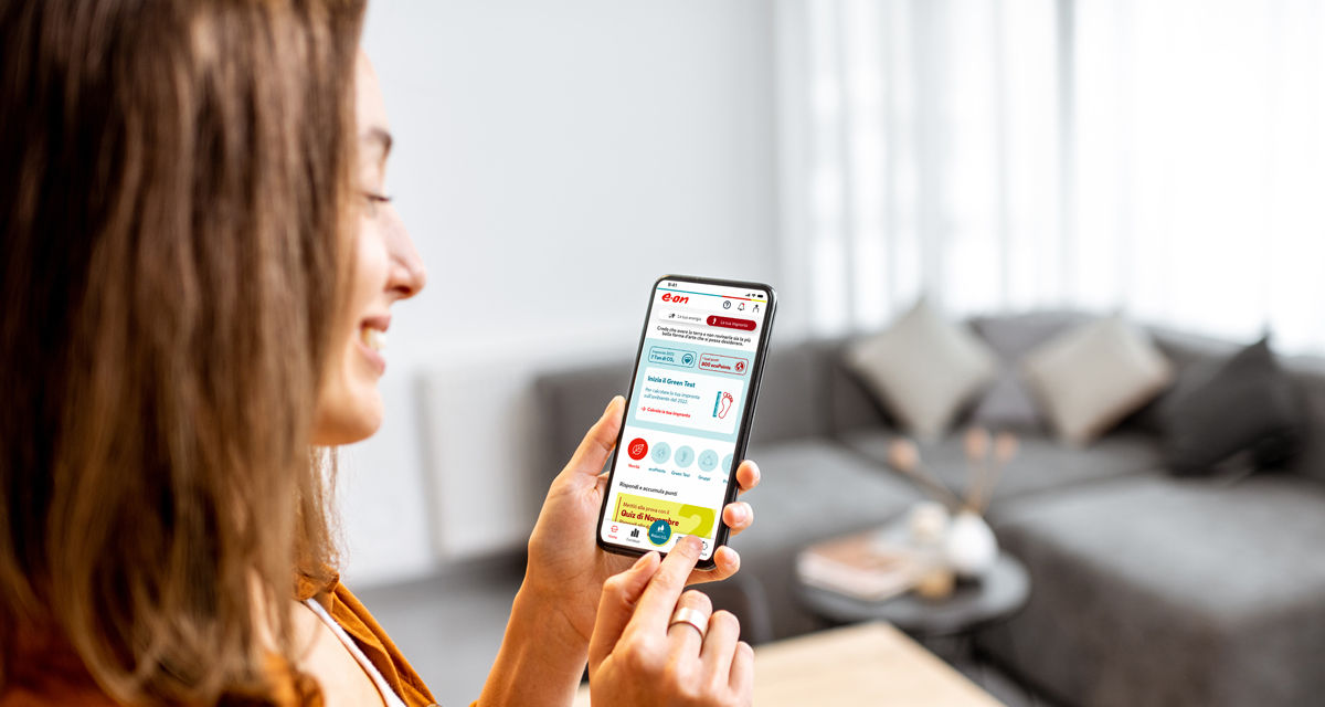 Una donna tiene in mano uno smartphone che mostra l'interfaccia rinnovata e 'più green' dell'App E.ON