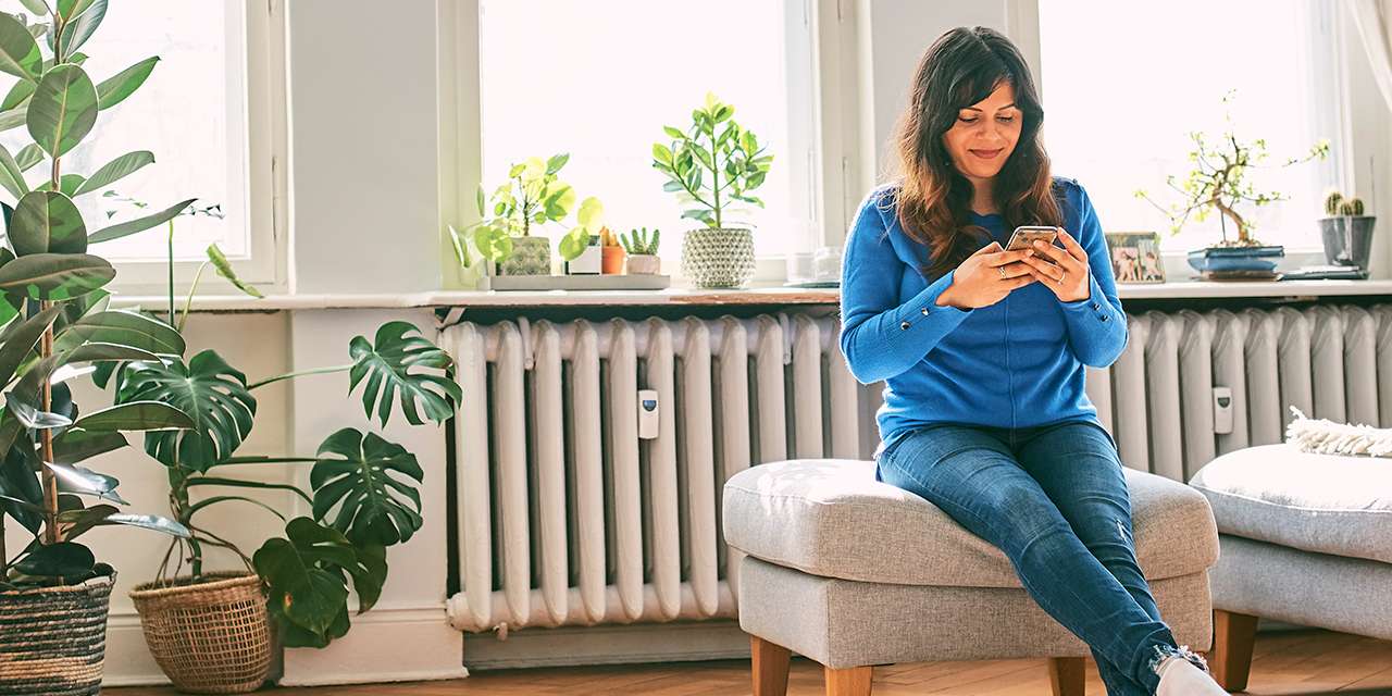 Una donna consulta lo smartphone in un soggiorno con un grande termosifone: si può scaldare casa senza sprechi energetici