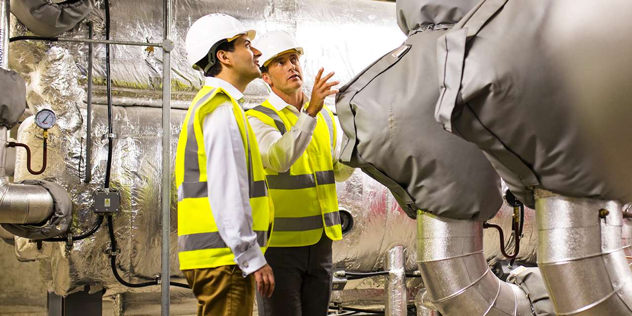 Due lavoratori con abbigliamento antinfortunistica si confrontano accanto a macchinari