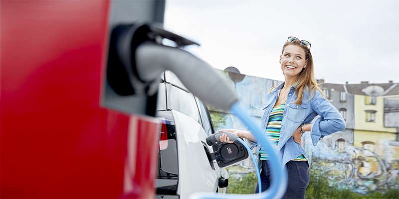 Una ragazza sorride e ricarica un’auto elettrica: la ricarica sulle colonnine pubbliche grazie a E.ON è un passo avanti verso la mobilità sostenibile