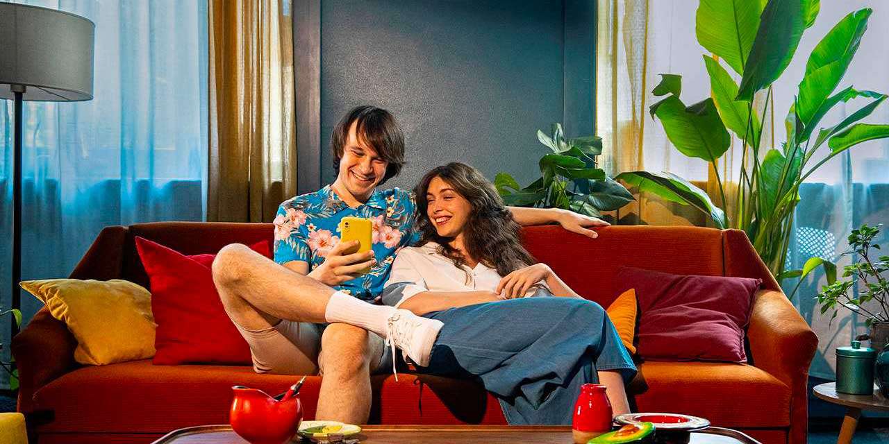 Una giovane coppia su un divano consulta lo smartphone ed è soddisfatta per l’ottenimento del bonus condizionatori