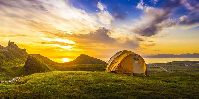 Una tenda montata in un paesaggio al tramonto: campeggio e cicloturismo rendono le vacanze green
