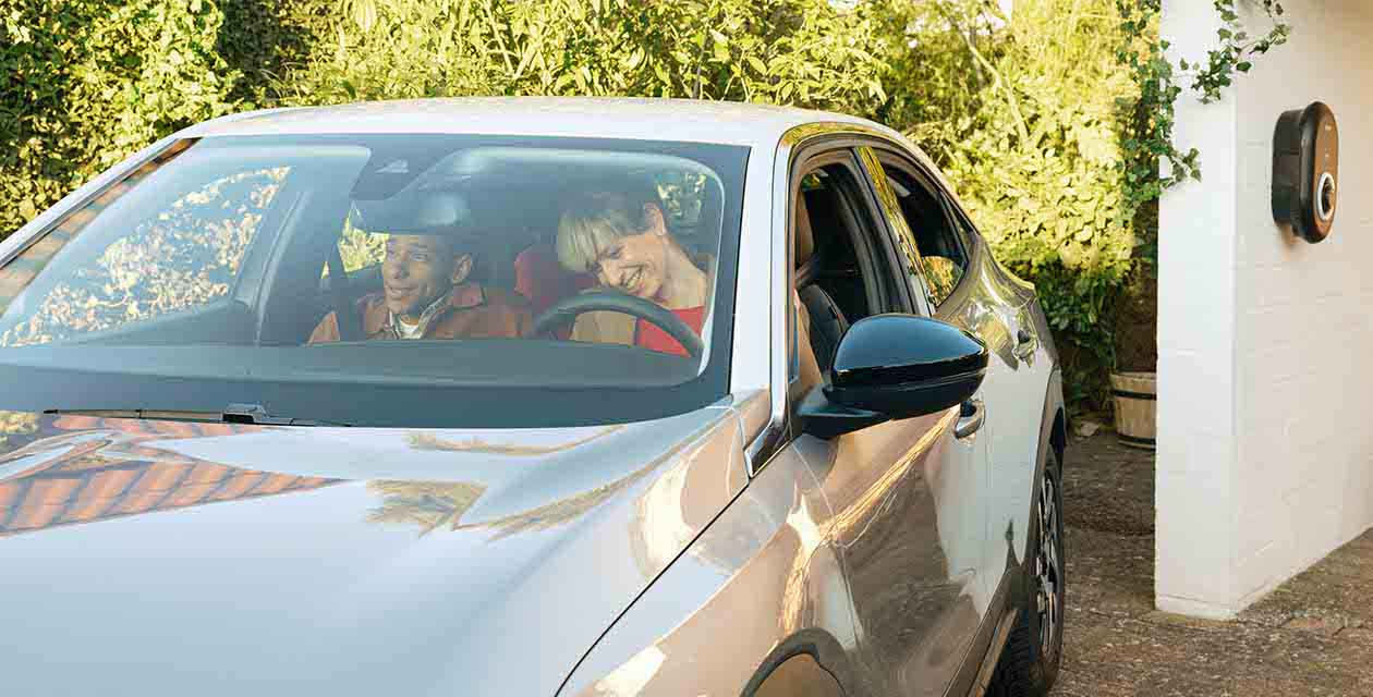 Una coppia sorridente in macchina si prepara a partire dopo aver ricaricato l’auto elettrica