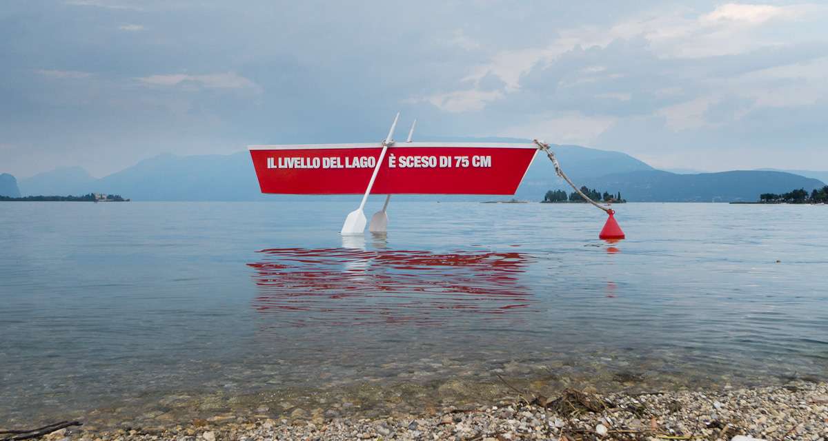 Una barca sospesa sulla superficie dell’acqua del Lago di Garda, a simboleggiare la siccità e i cambiamenti climatici