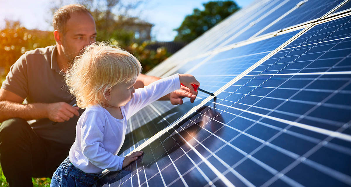 Un bambino col papà gioca accanto a pannelli fotovoltaici: anche il fotovoltaico può giovarsi del riciclo e dell’economia circolare