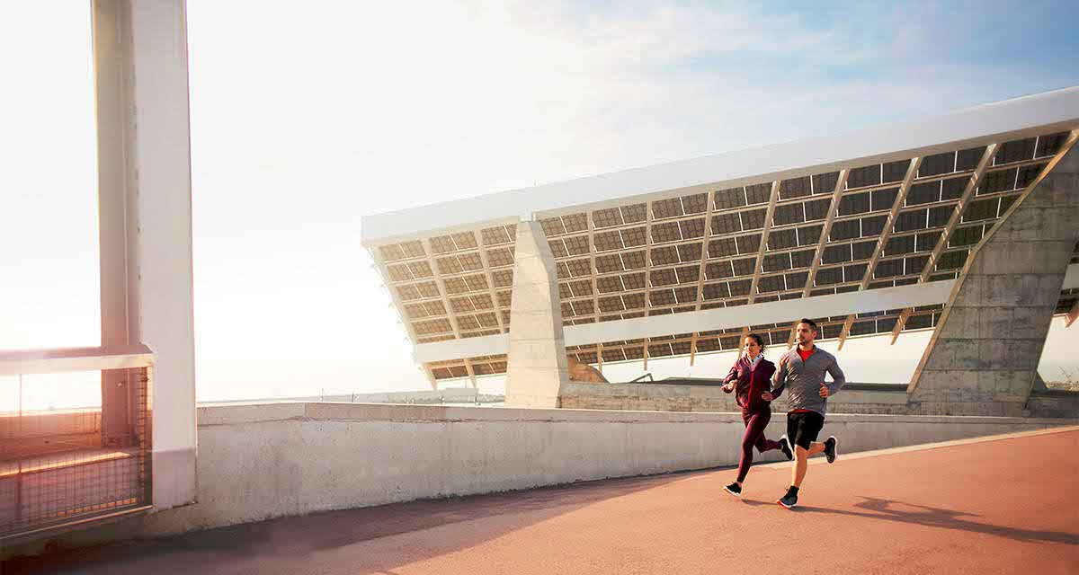 Due persone si allenano correndo in un impianto sportivo moderno: le nuove strutture sono attente alla riqualificazione energetica