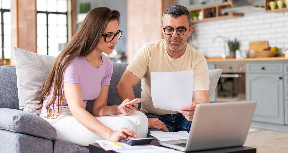 Una coppia, seduta sul divano in un soggiorno, controlla smartphone e computer.