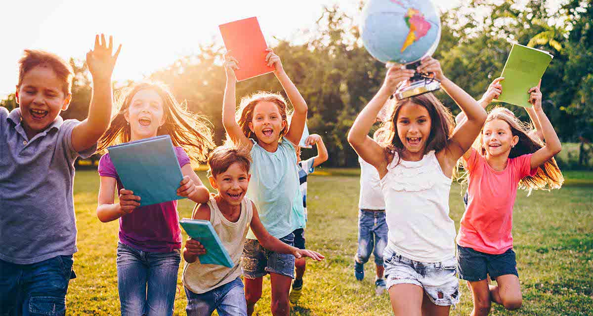 Bambini corrono su un prato con un mappamondo e cartoncini colorati in mano