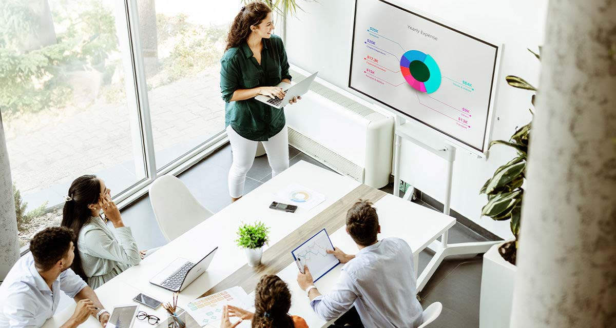 Una giovane donna illustra dei grafici su una lavagna a quattro colleghi in uno studio bianco e luminoso