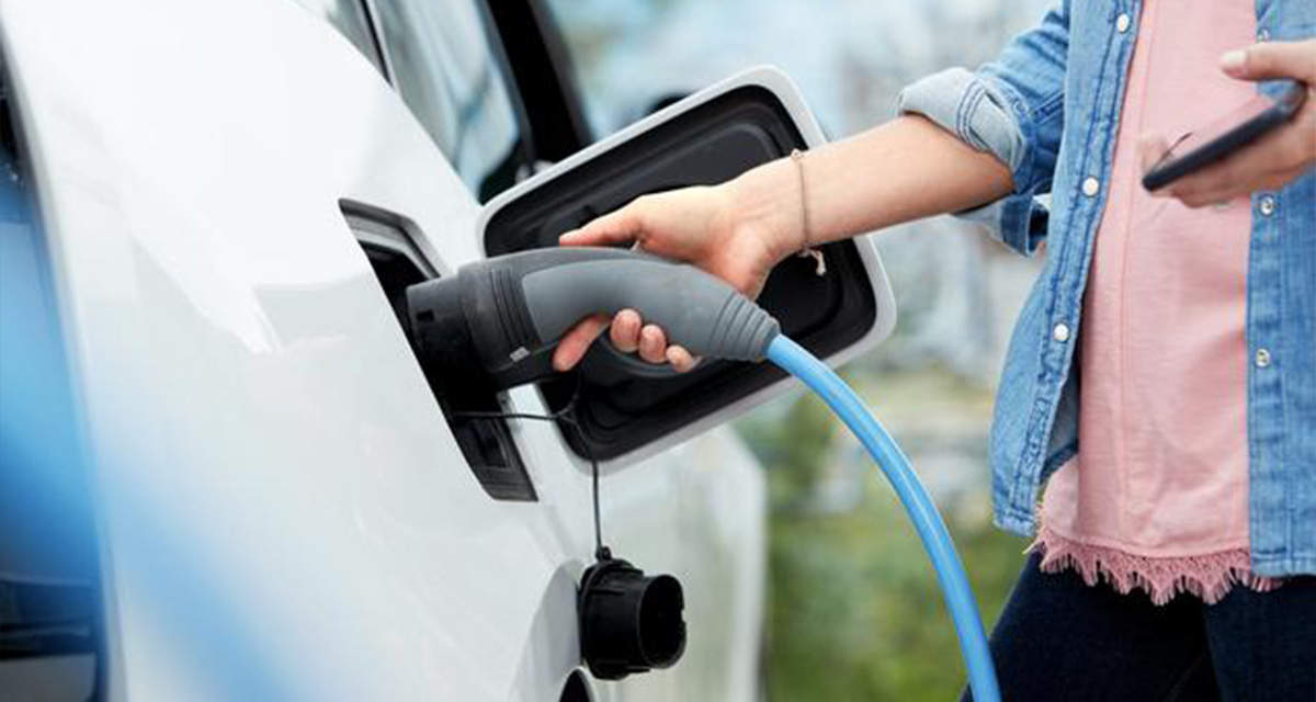 Una ragazza fa il pieno alla propria auto presso una colonnina di ricarica per veicoli elettrici