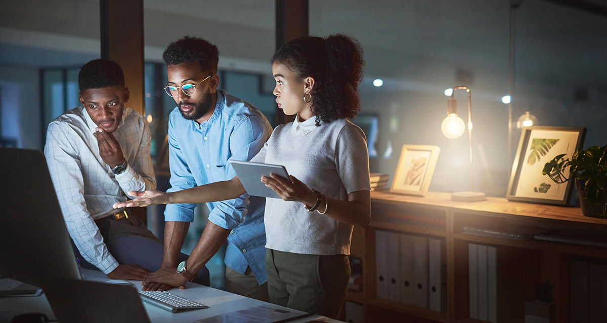 Una giovane donna illustra a due giovani uomini dei dati su alcuni dispositivi, durante un incontro di lavoro