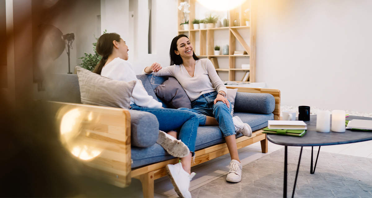 Due amiche sorridono e parlano su un divano in un soggiorno