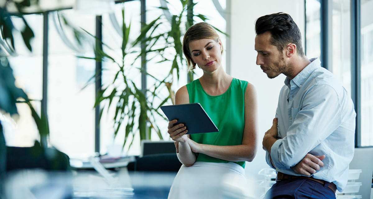 Una giovane donna mostra a un collega alcuni dati su un tablet: le certificazioni ambientali sono sempre più importanti per le aziende