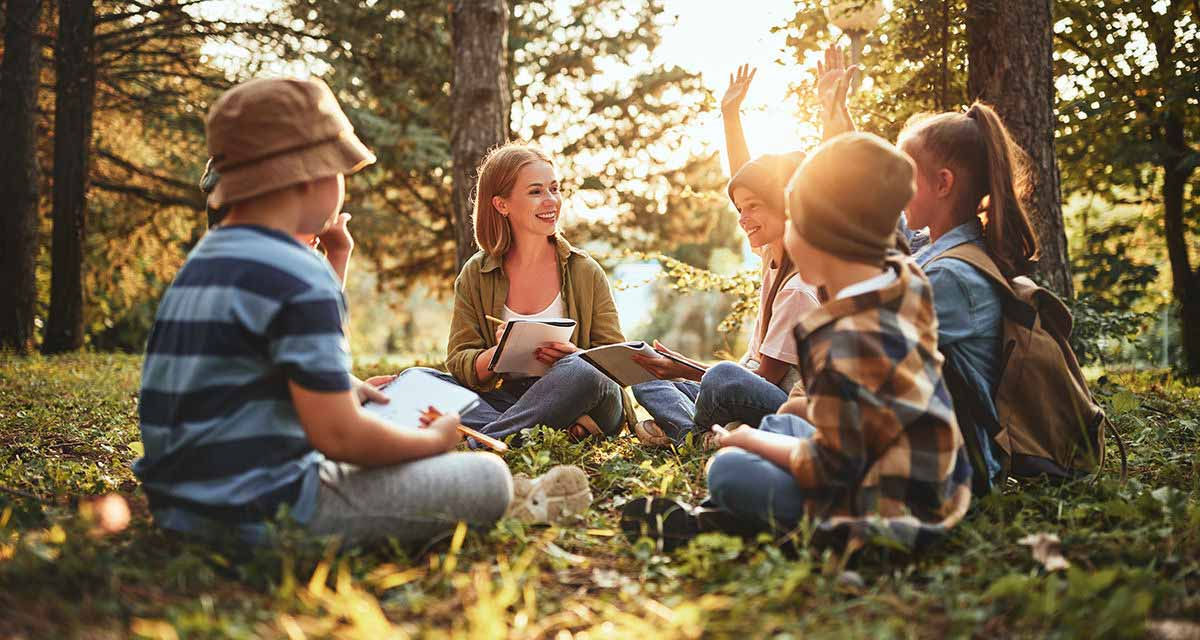 Un gruppo di ragazzi studia con la propria insegnante in un bosco