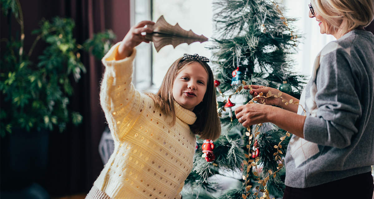 Una bambina gioca con le decorazioni natalizie accanto alla mamma e all’albero di Natale