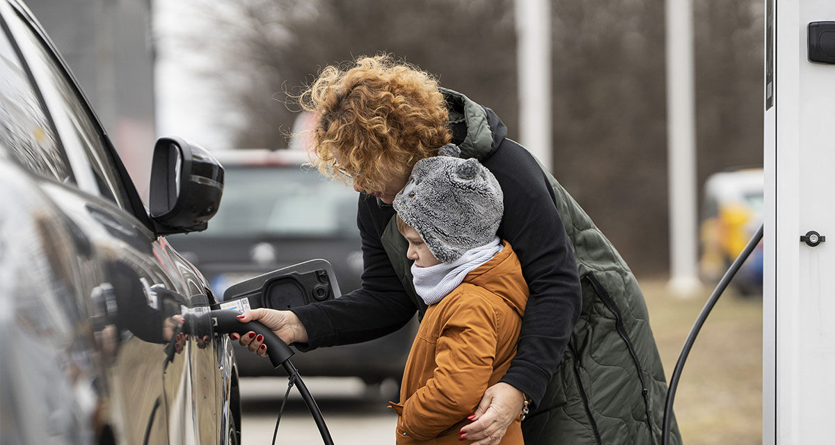 Una mamma con il figlio ricarica l’auto elettrica in una stazione pubblica