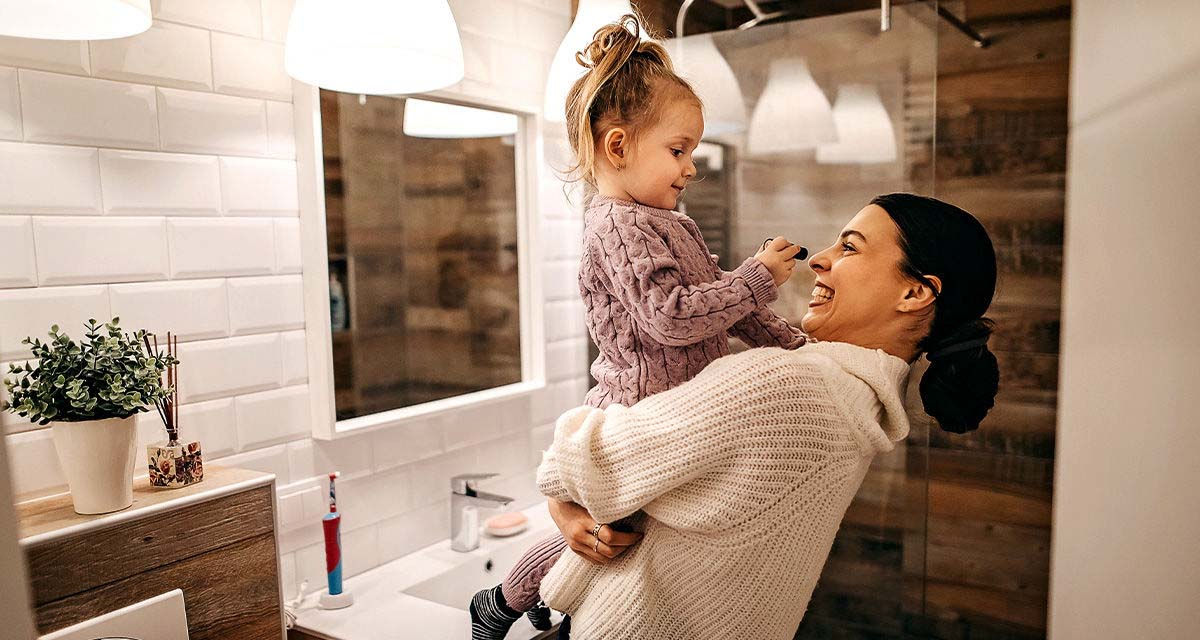 Una mamma gioca con la figlia piccola in braccio in un bagno luminoso