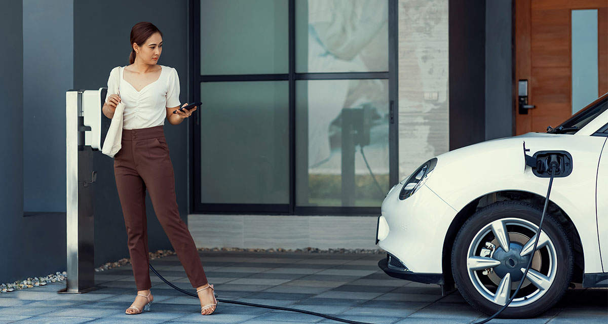 Una ragazza ricarica la propria auto elettrica in una stazione di ricarica domestica