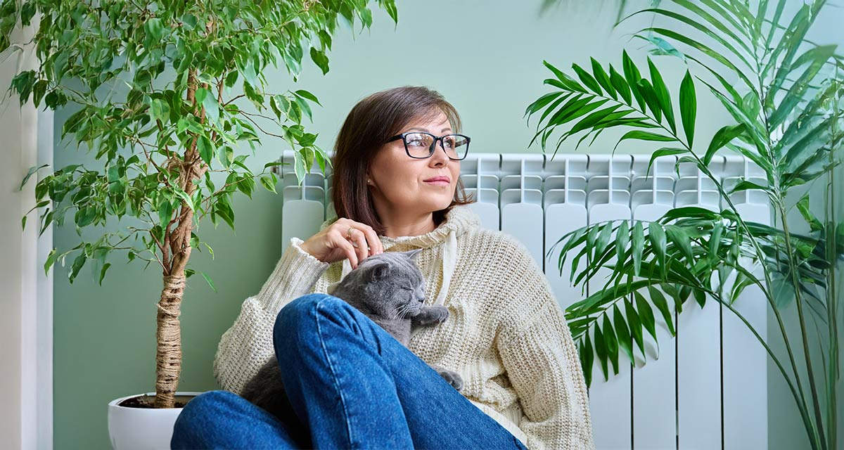 Una donna con un gatto siede accanto a un termosifone in alluminio