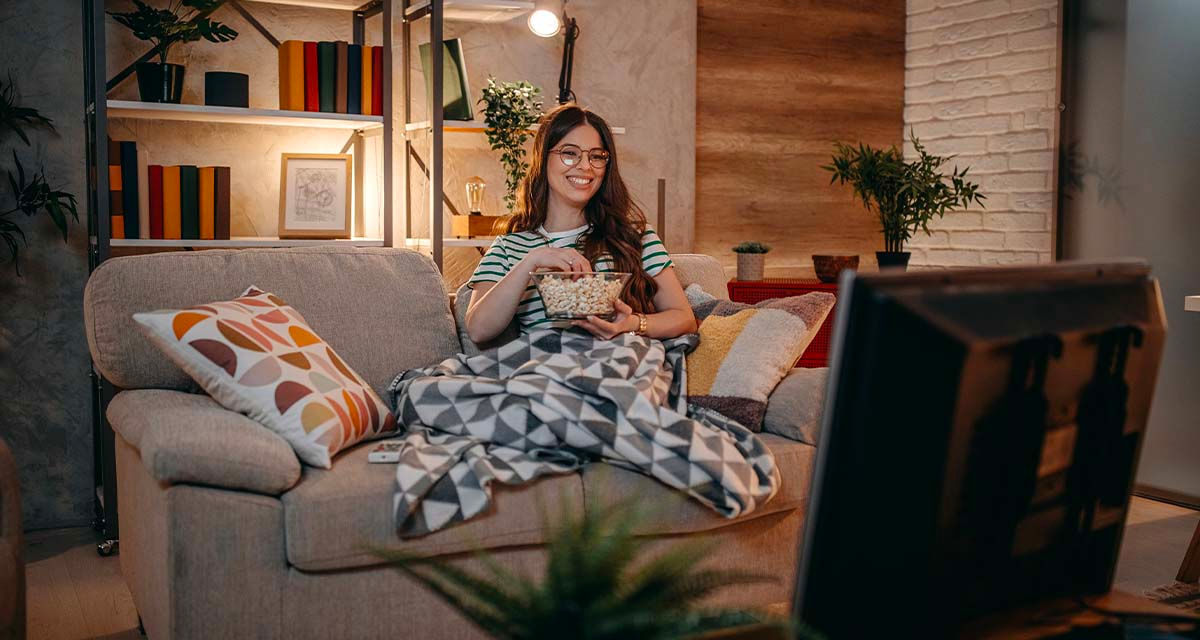Una ragazza sorride sul divano, in un soggiorno illuminato: la tariffa trioraria fa risparmiare chi concentra i consumi nelle ore serali