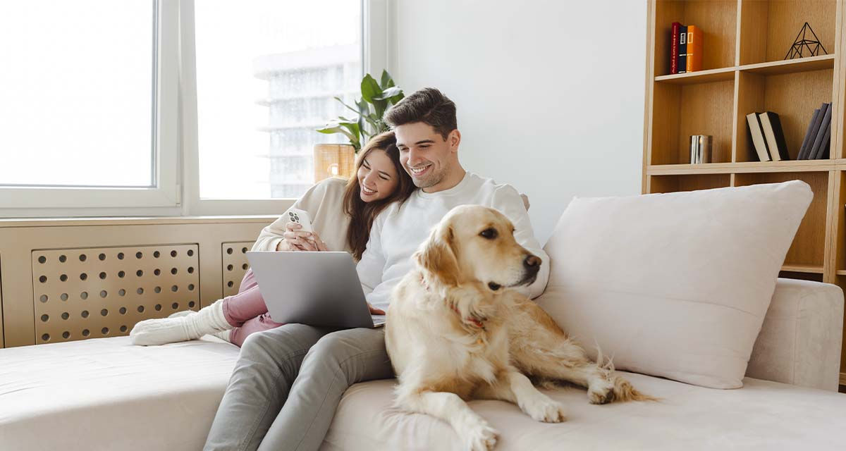 Una giovane coppia con un cane sfrutta l’abbondante illuminazione naturale per rilassarsi su un divano, rimandando i consumi elettrici a orari serali